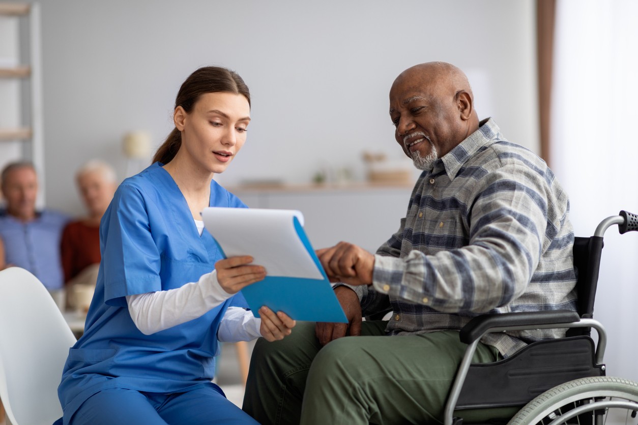 A nurse talking to an older African American man sitting in a wheelchair.